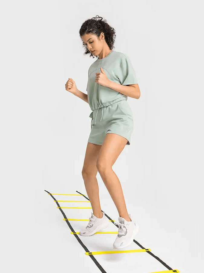 Woman exercising in a sports short sleeves crop T-shirt with adjustable hem, demonstrating agility on a training ladder.